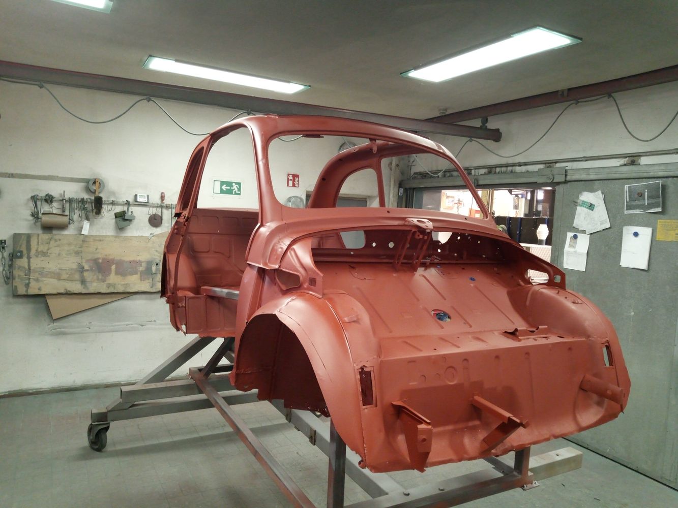 Eine unfertige orangefarbene Karosserie auf einem Rollgestell in einer Werkstatt, umgeben von Werkzeugen und Geräten